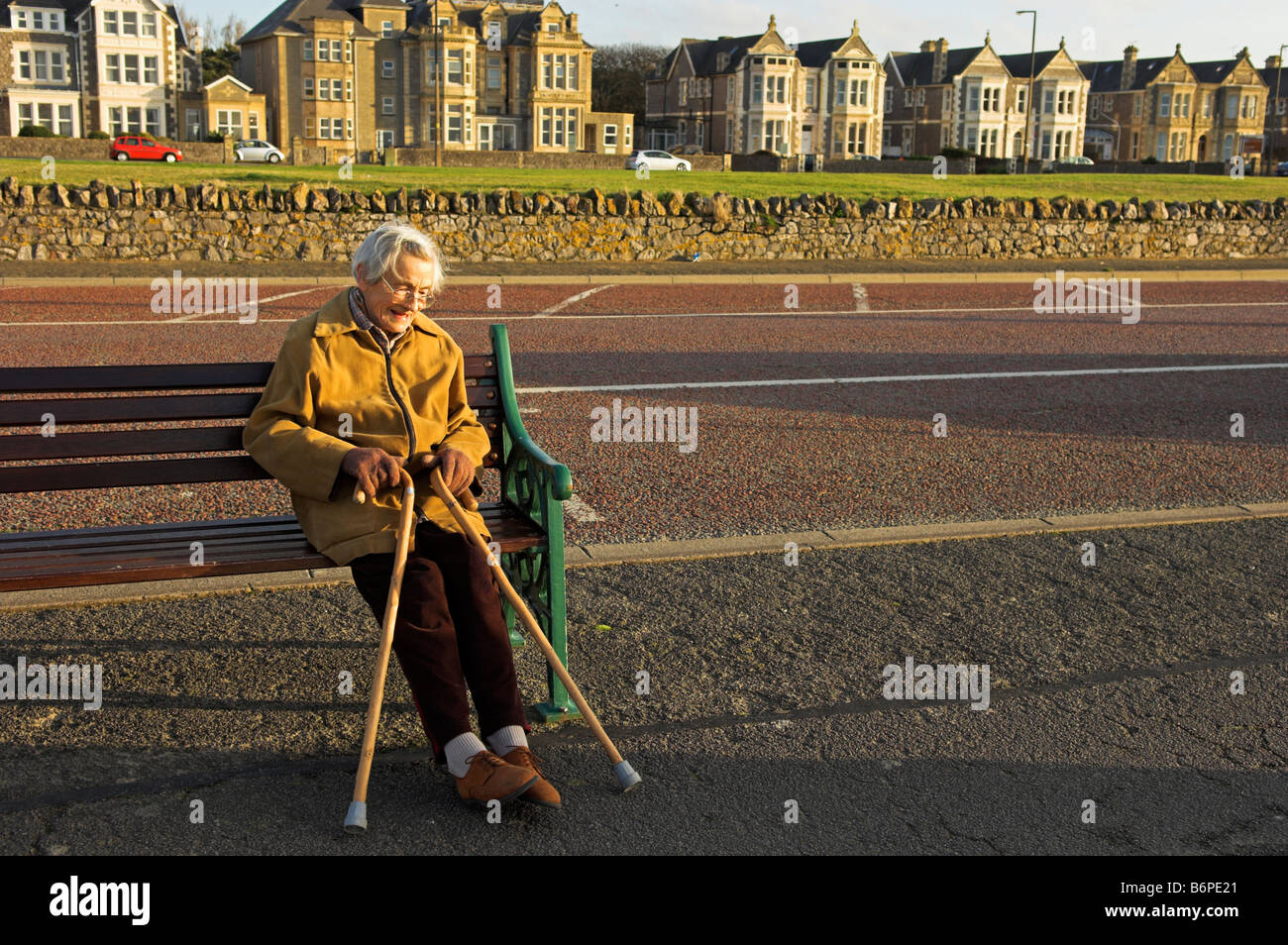 Elderly woman sitting on bench in late afternoon winter sun Weston Super Mare North Somerset England Stock Photo