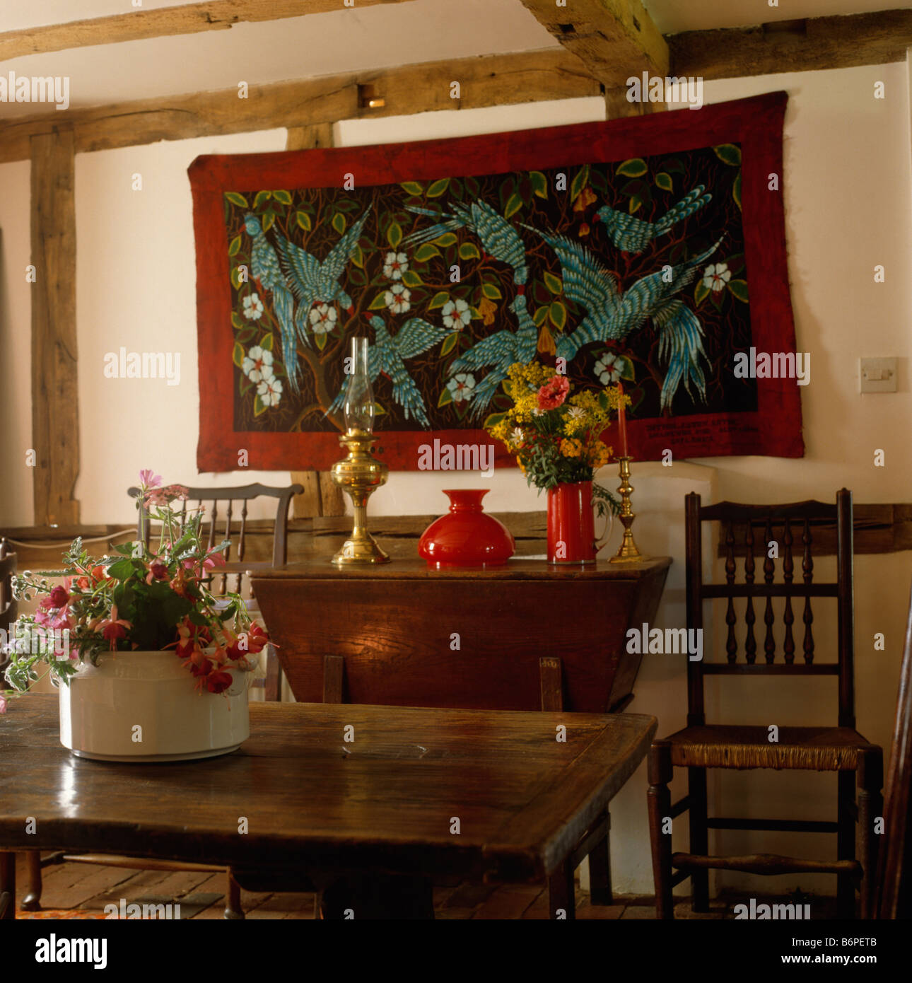 Appliqued wall hanging on wall above antique console table in beamed cottage dining room Stock Photo
