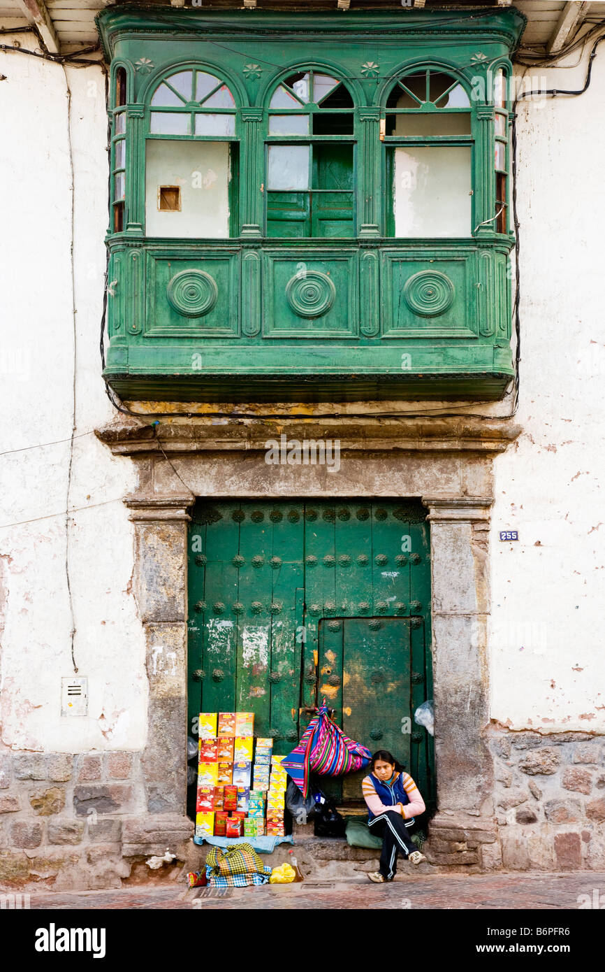 Young Peruvian woman selling goods in doorway of Spanish colonial house down a side street in Cusco, Peru, South America Stock Photo