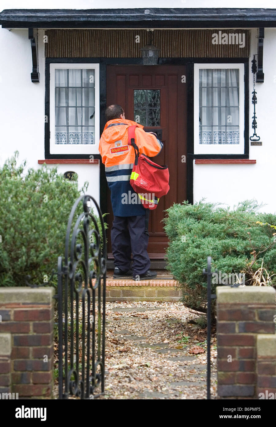 A Royal Mail postman delivers letters through a door on his round in Essex U K Stock Photo