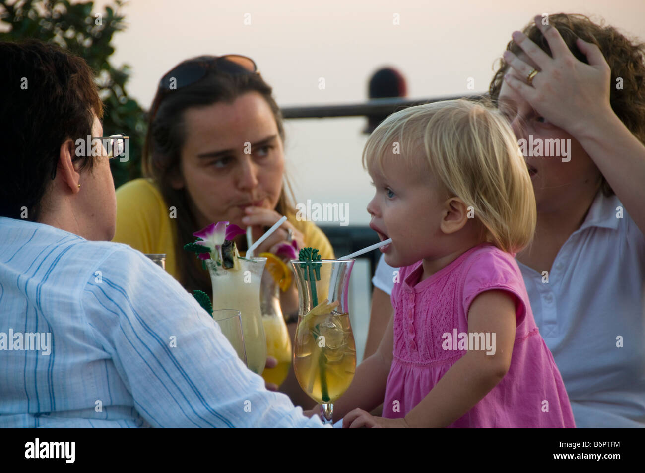 little girl sipping her drink at sunset on a rooftop bar in Bangkok Thailand Stock Photo