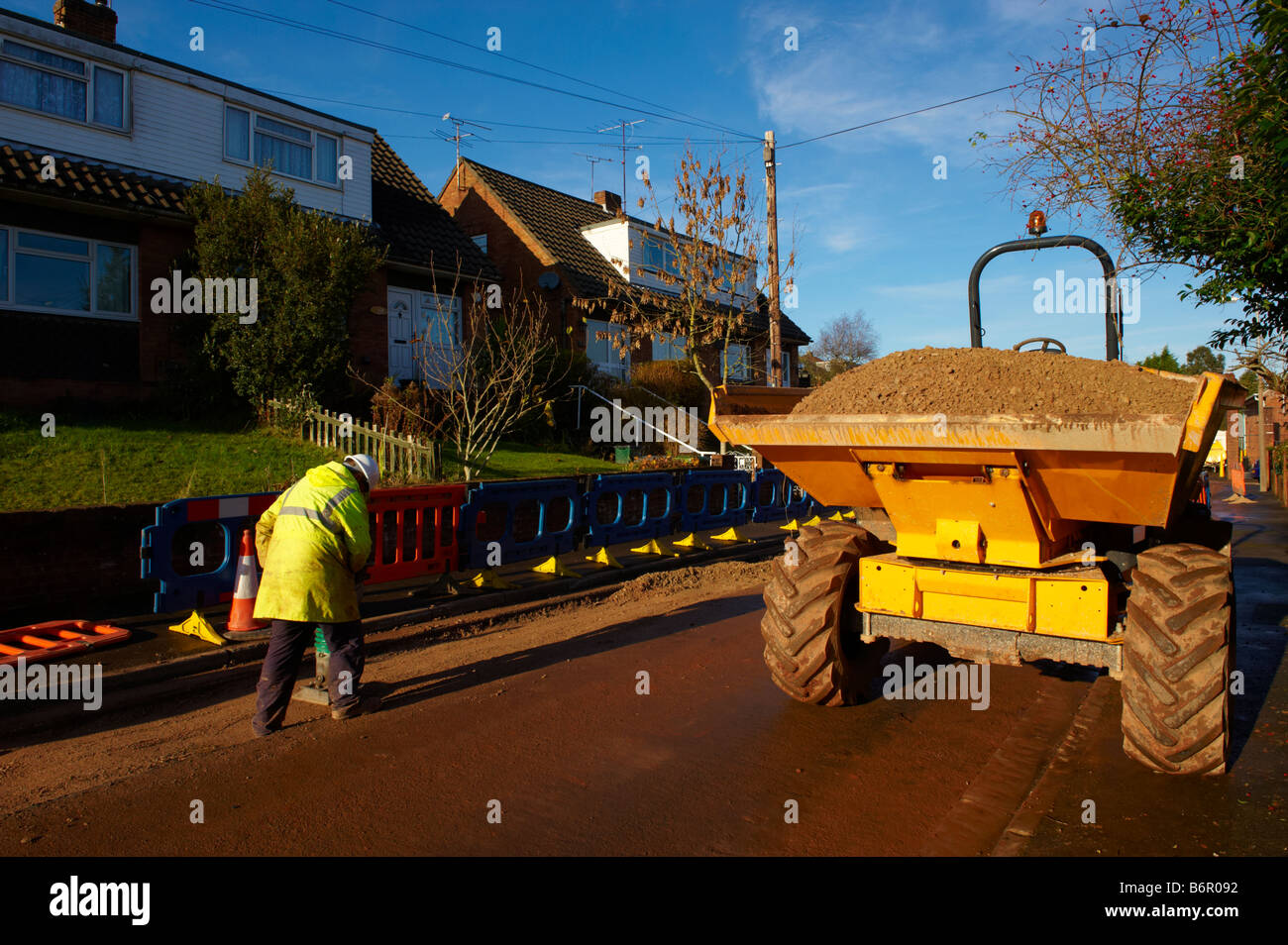 Workman using heavy duty pounder to pound gravel in road after laying electrical cabling with dumper truck parked on road Stock Photo