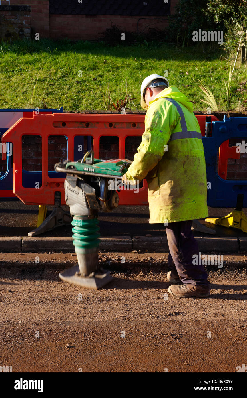 Workman using heavy duty pounder to pound gravel in road after laying electrical cabling Stock Photo