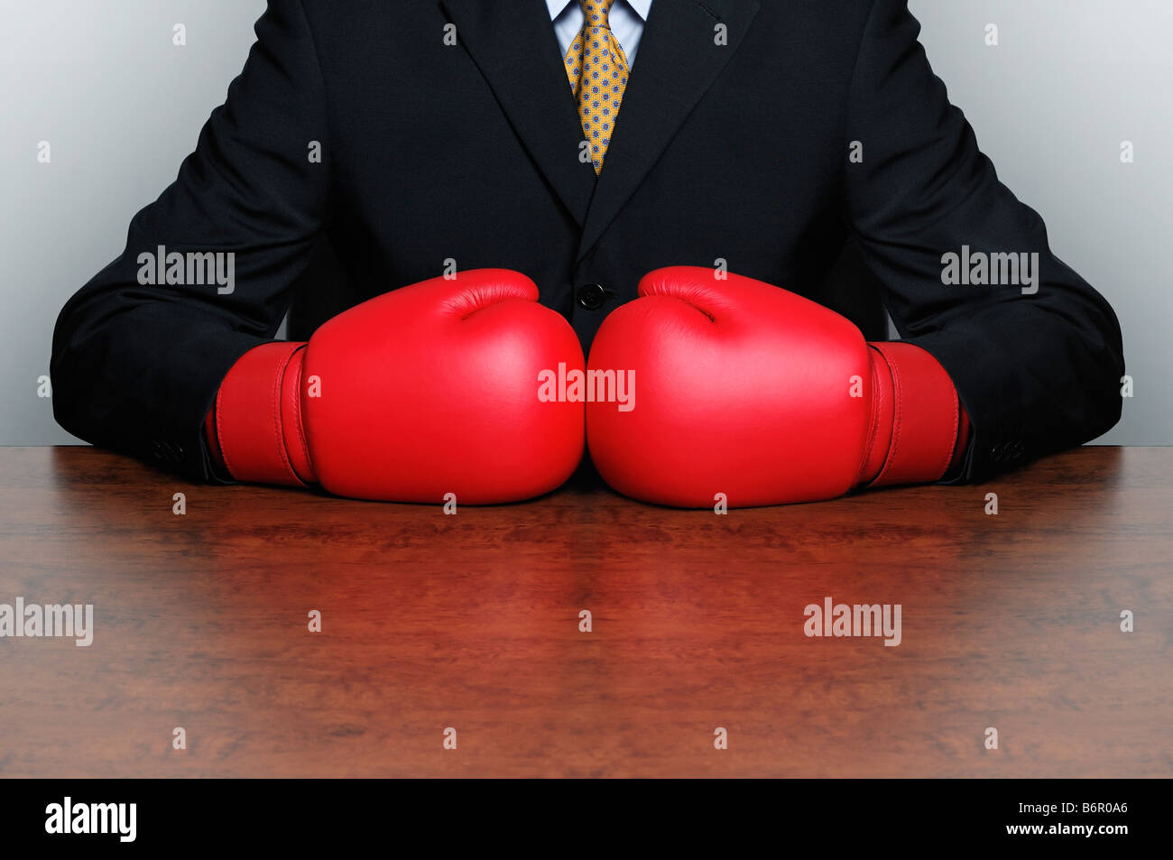 Businessman Wearing Boxing Gloves Sat Behind a Desk in an Office Stock