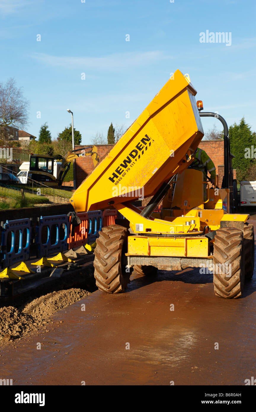 Workman using dumper truck to tip gravel into hole in road after laying electrical cabling Stock Photo
