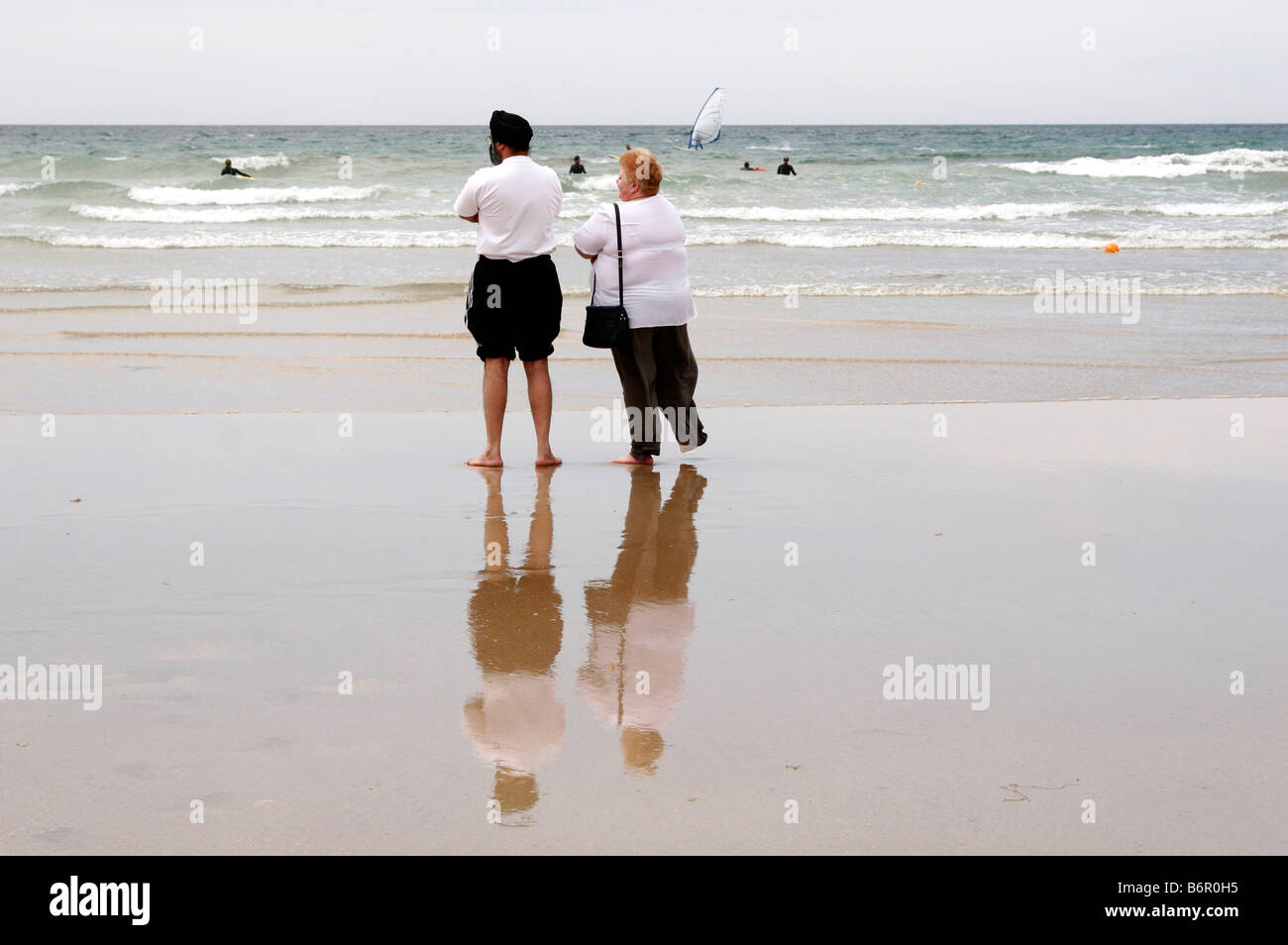 Man and woman standing on a sandy beach watching surfers, swimmers and ...