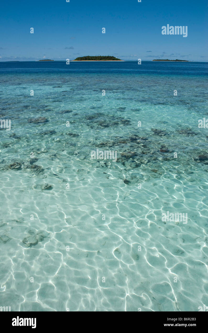 Small tropical islands in the Maldives and clear shallow water over coral reef in the foreground. Stock Photo