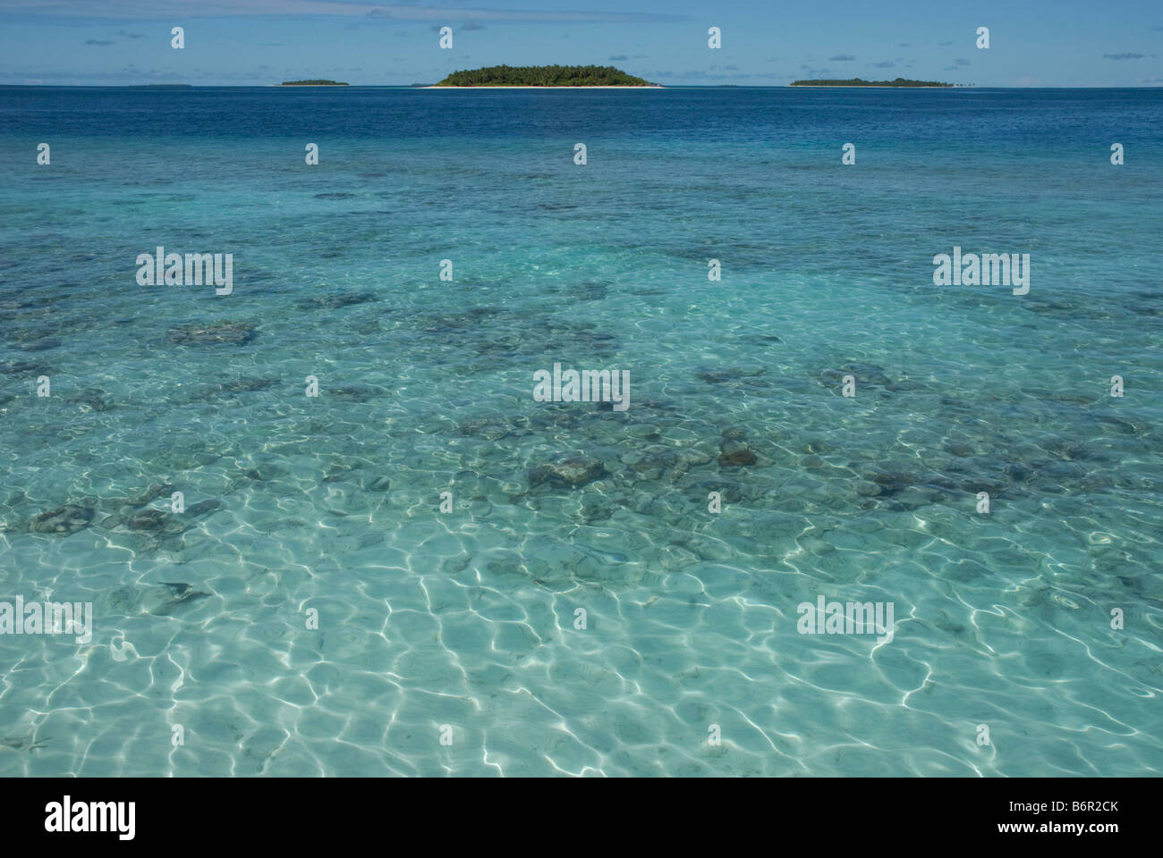 Small tropical islands in the Maldives and clear shallow water over coral reef in the foreground. Stock Photo