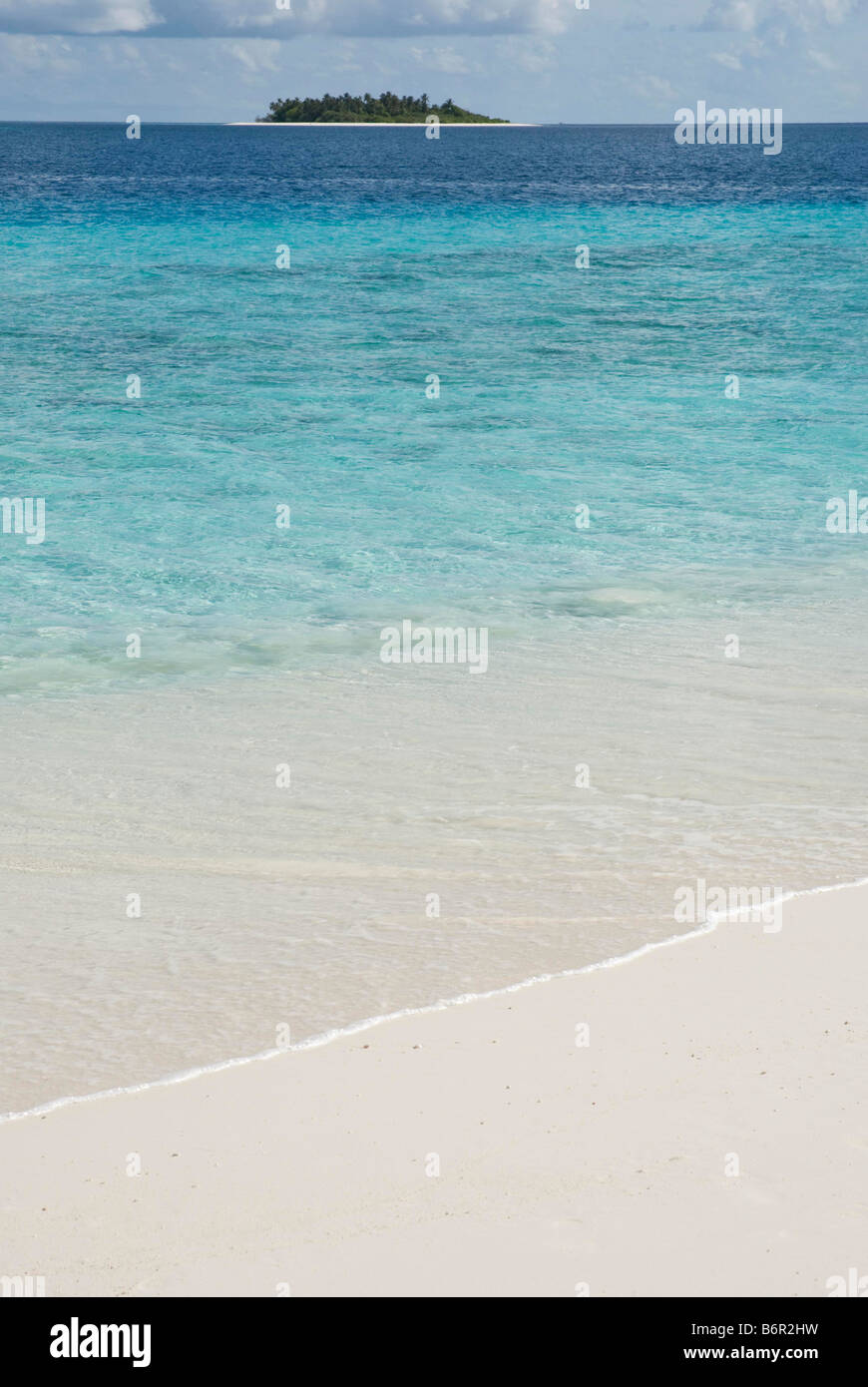 Small uninhabited tropical island in the Maldives and sand and turquoise coloured shallow water in the foreground. Stock Photo