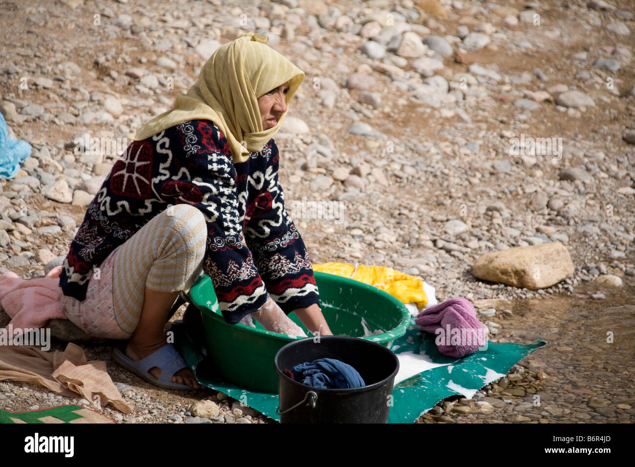woman washing clothes in bucket by river. head shawl Marakkesh Morocco