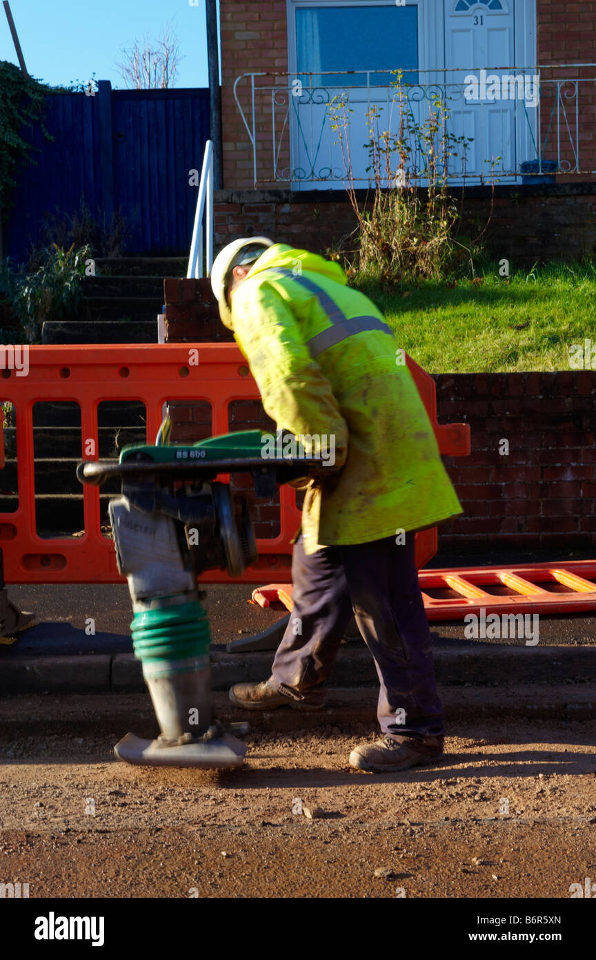 Workman using heavy duty pounder to pound gravel in road after laying electrical cabling Stock Photo