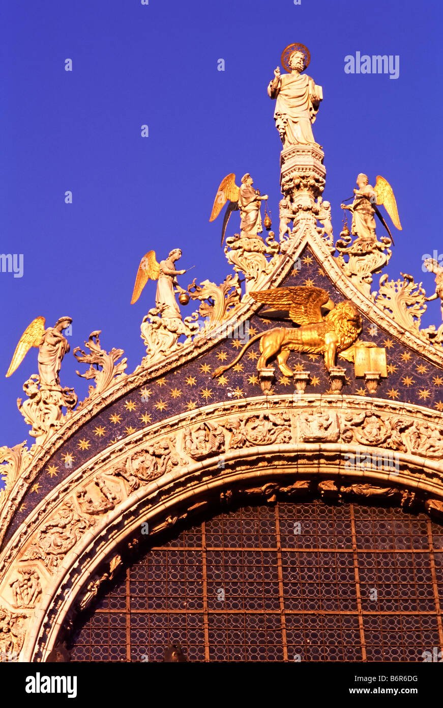 Above the large central window of the façade of St. Mark's Basilica, St Mark watches over the city and the Winged Lion. Stock Photo