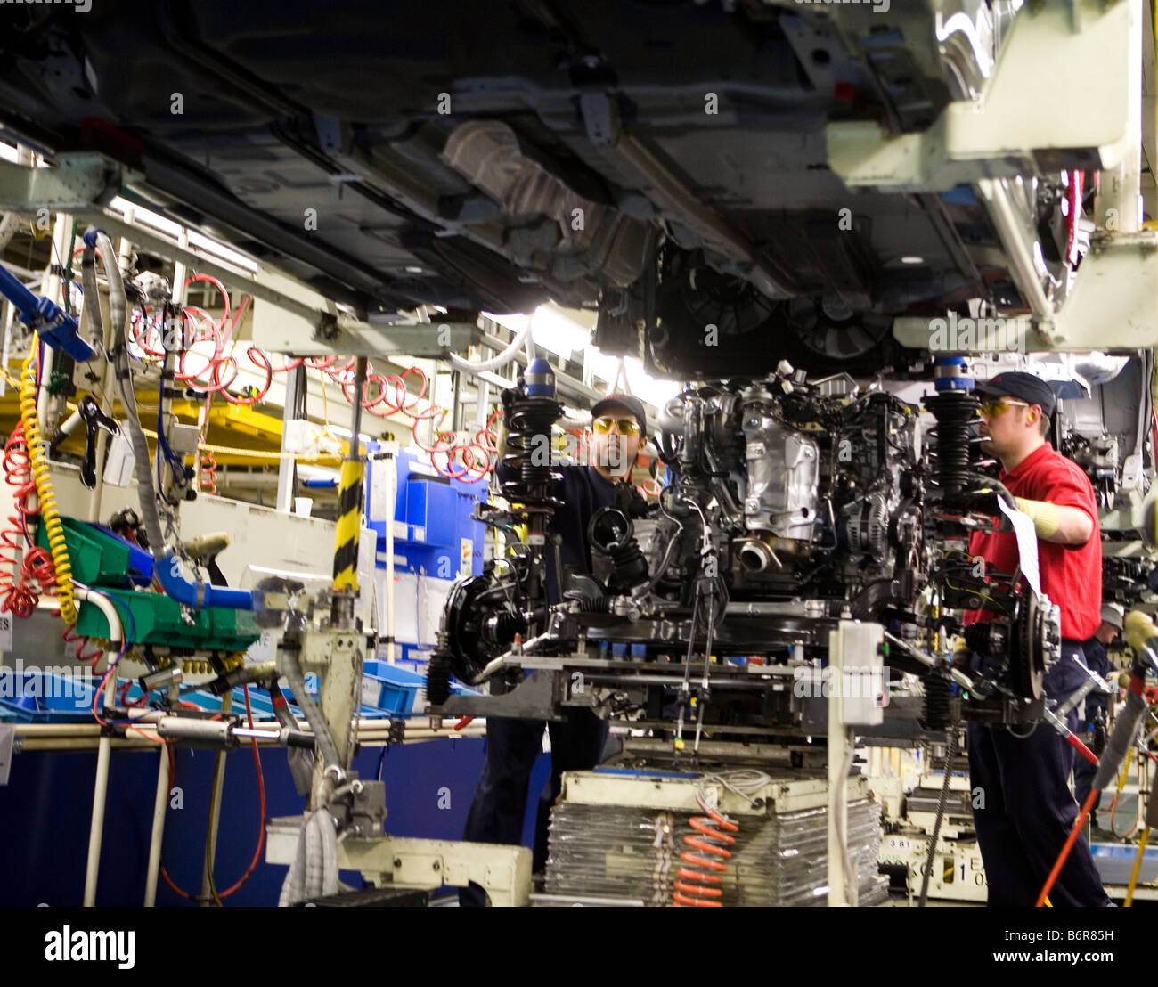 Workers at Toyota Final Assembly production line prepare the engine for installation to the chassis of a Toyota Avensis car Stock Photo