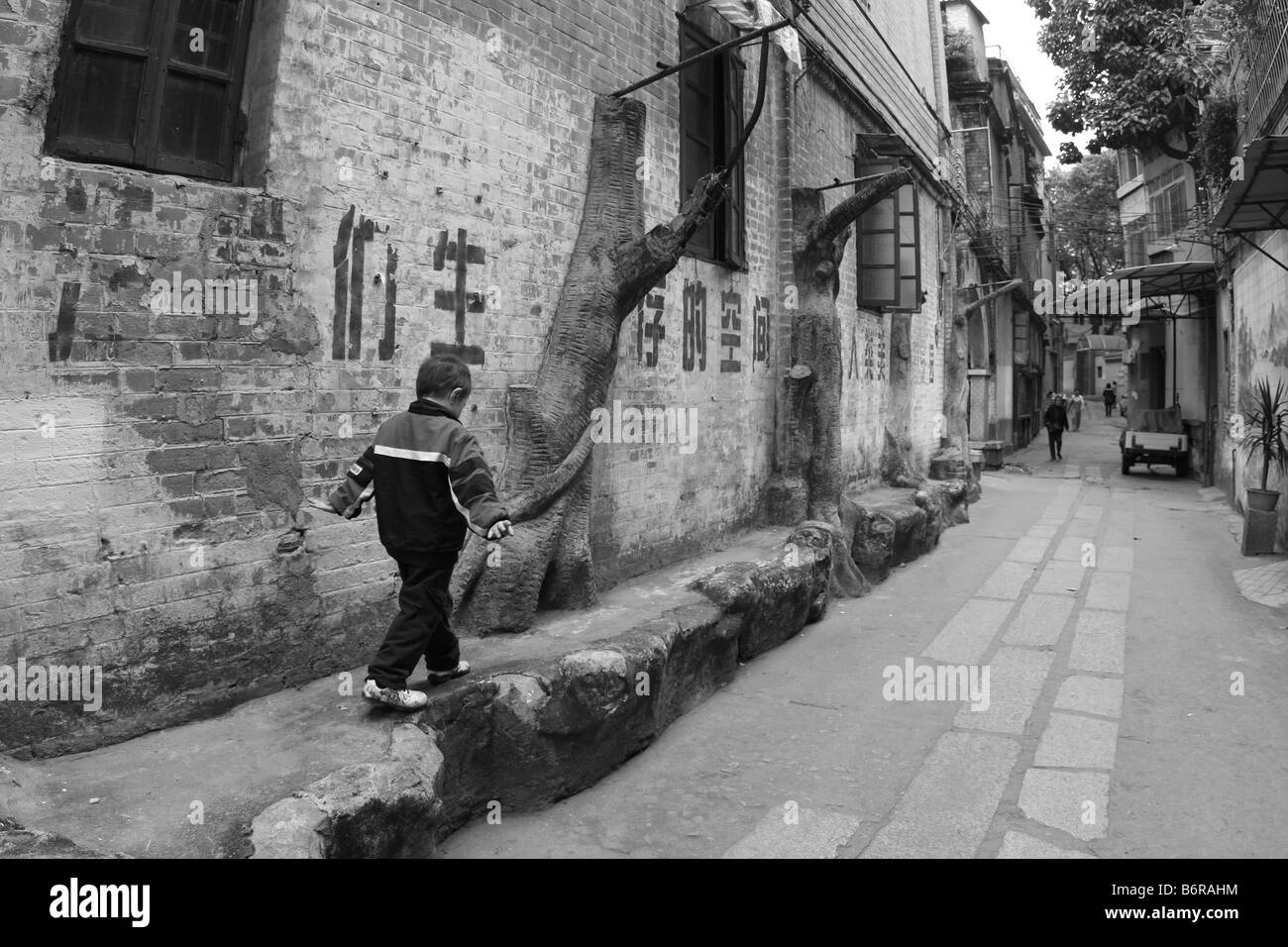 Chinese child playing on the side of house in Guangdong China Guangzhou Asia in front of fading communistic propaganda Stock Photo