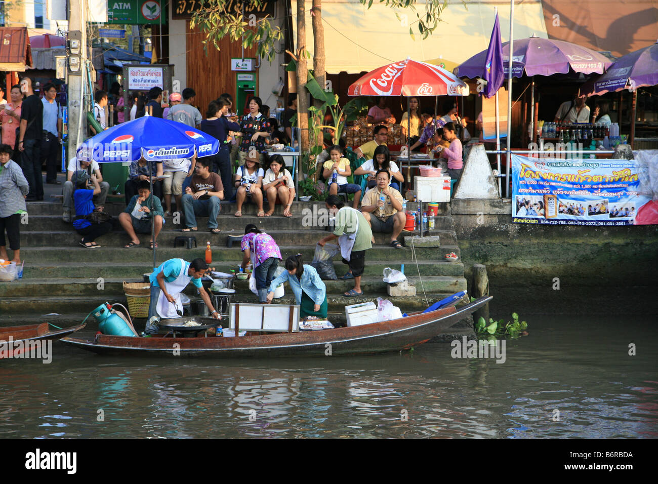 People preparing food on wooden boat serving people on the bank. From Amphawa Floating Market, Thailand Stock Photo