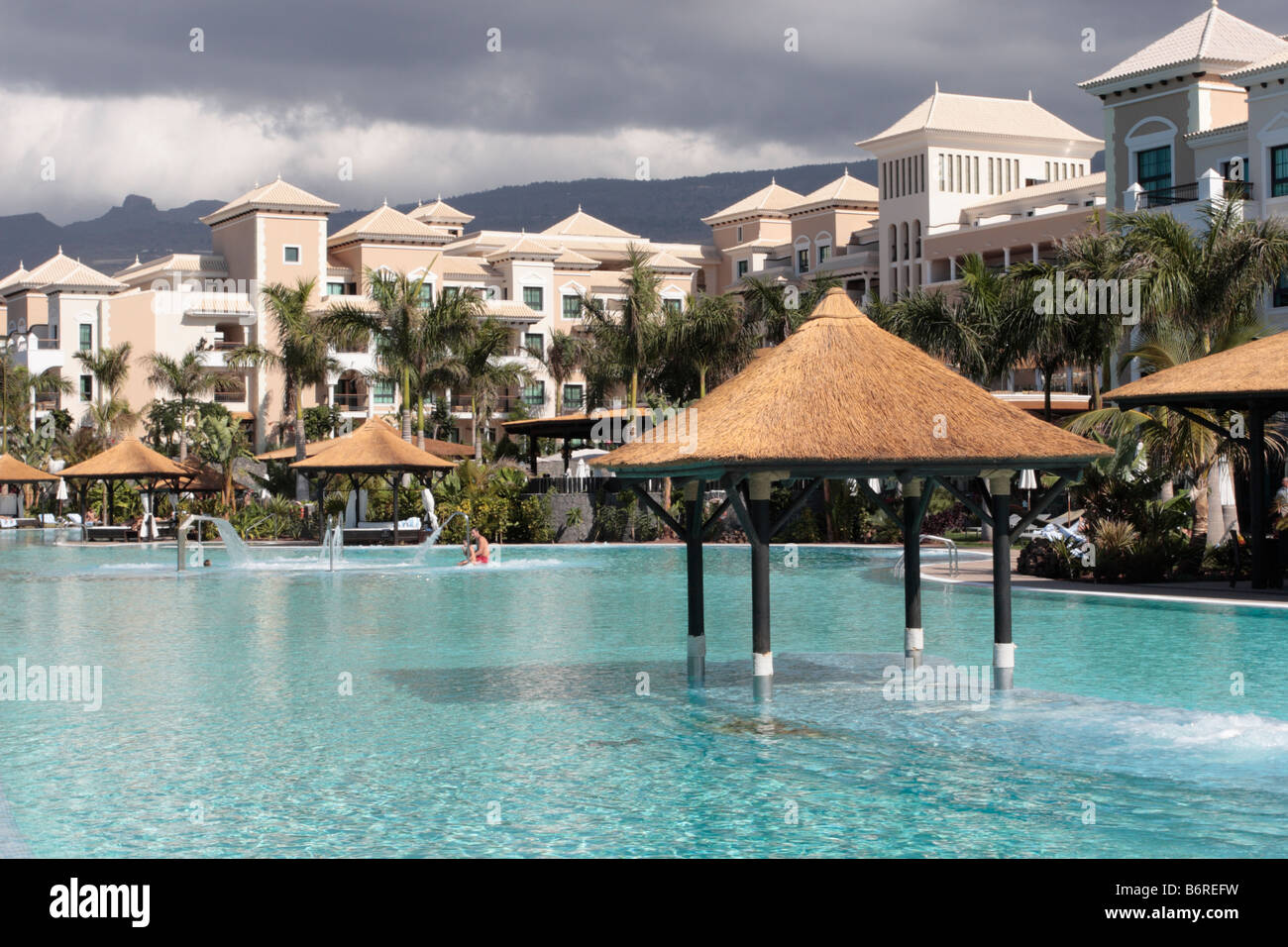 The pool area of the Sol Melia hotel Gran Palacio de Isora in sunshine whilst storm clouds appear over the mountains Stock Photo