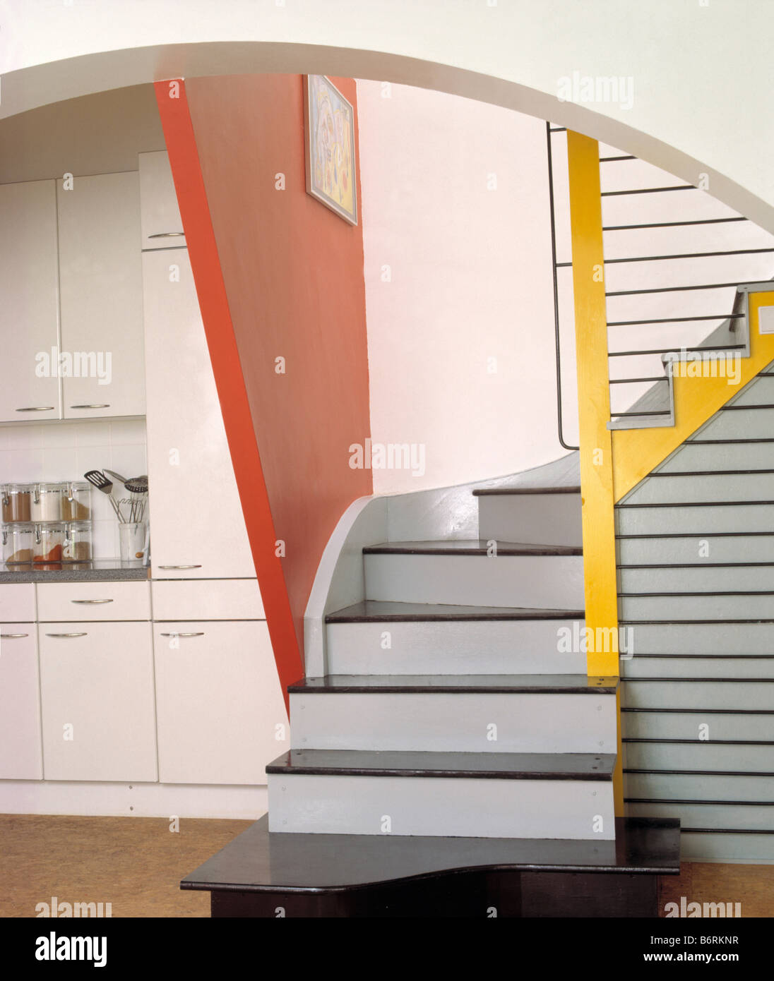 Grey staircase with yellow bannisters and red wall leading out of modern white kitchen Stock Photo