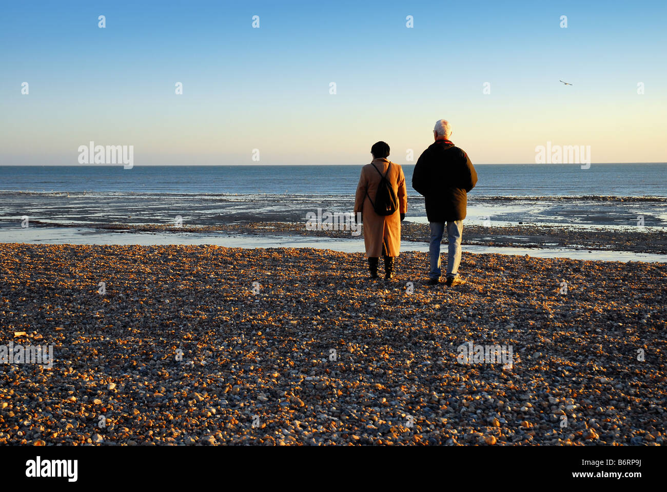 Two old people looking out to sea from beach Stock Photo