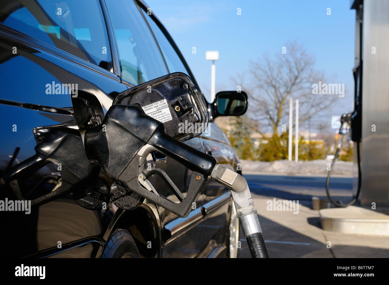 Gas pump nozzle inserted into a black car while refueling at a gas station in winter Stock Photo