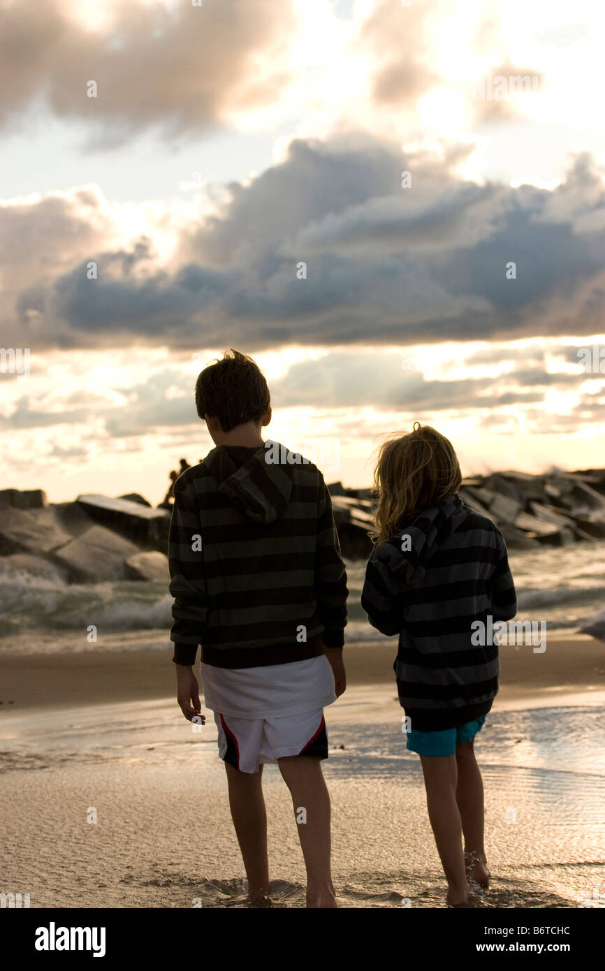 Young boy and girl walking near the surf and rocks at the beach ...