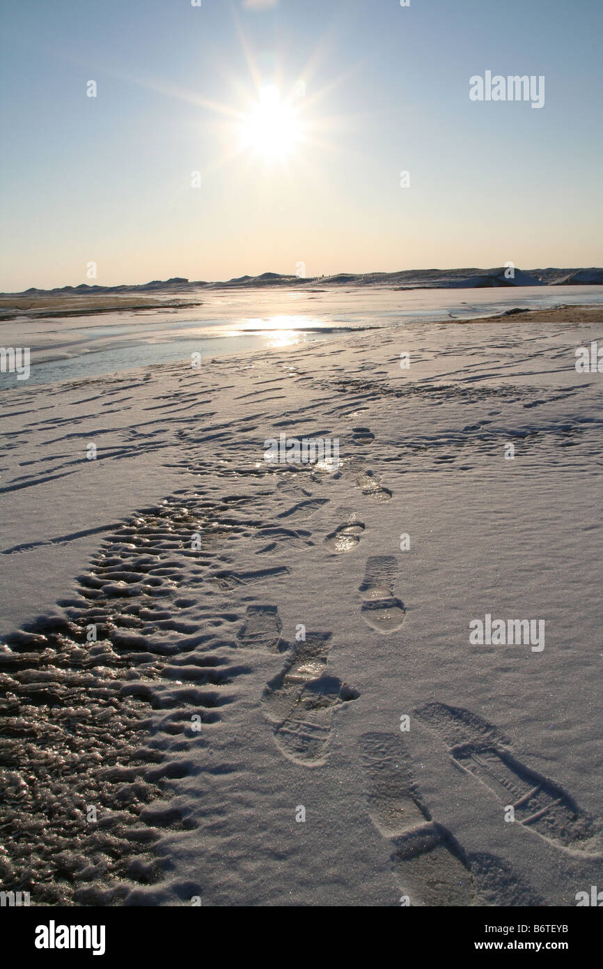 Footsteps in frozen landscape with setting sun in background Stock Photo