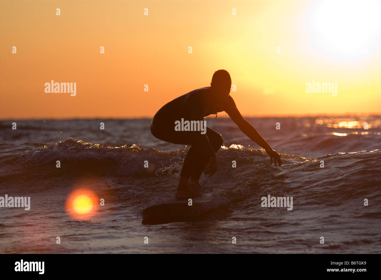 Surfer riding in on small wave at sunset on Lake Michigan Stock Photo