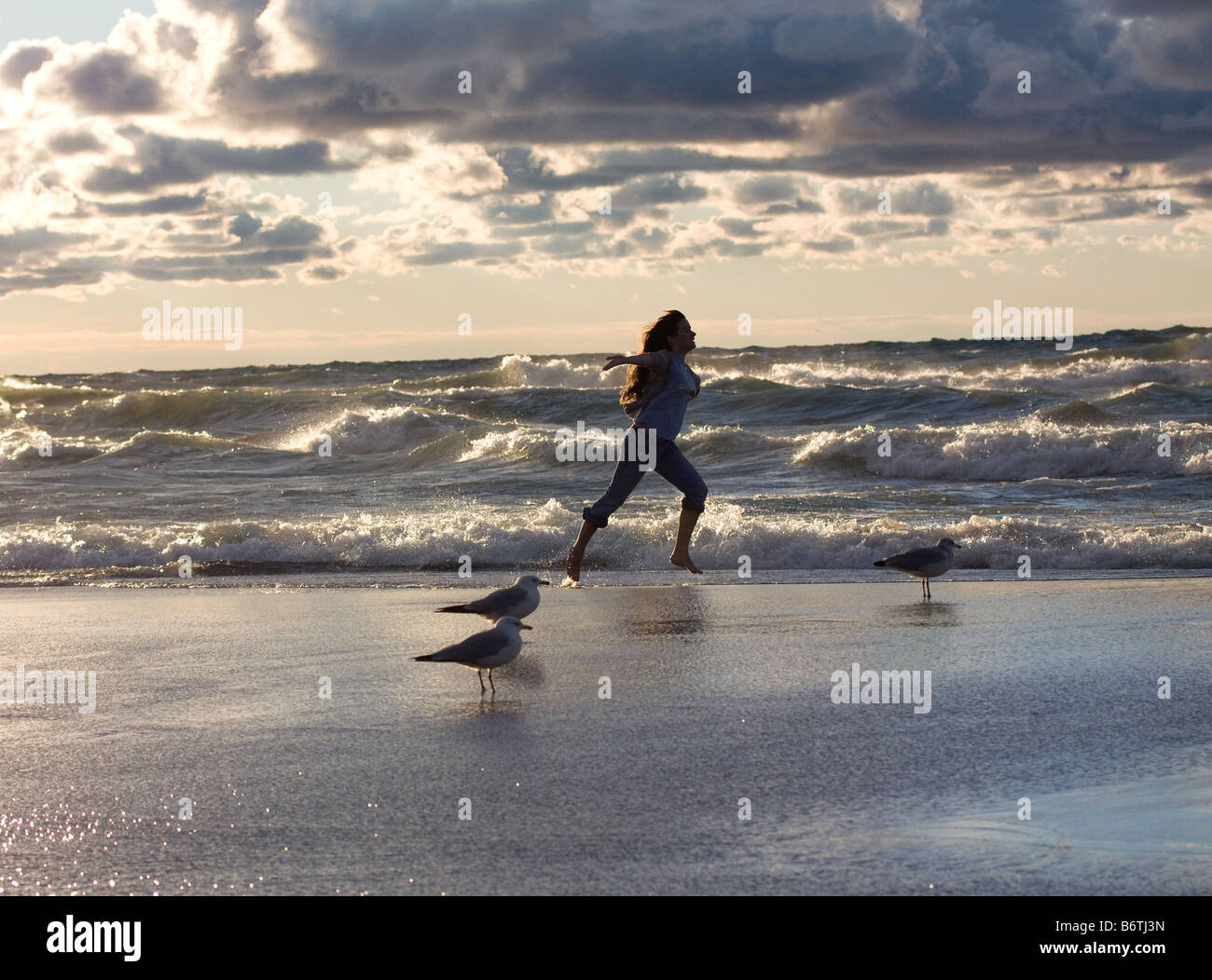 Girl running on beach near shore with seagulls Stock Photo