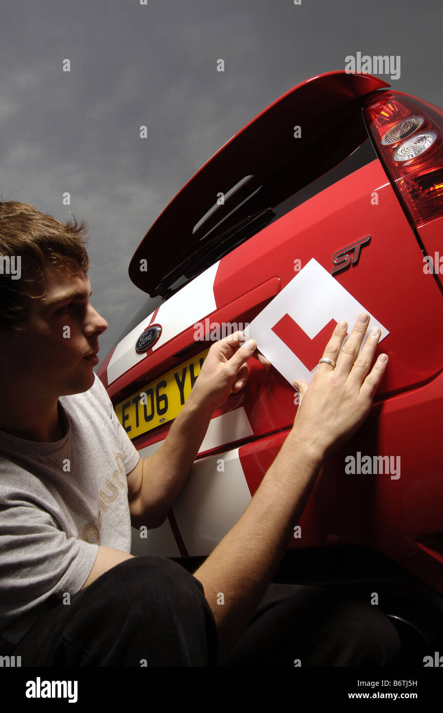 student l earner driver puts l plates on a red car. Stock Photo