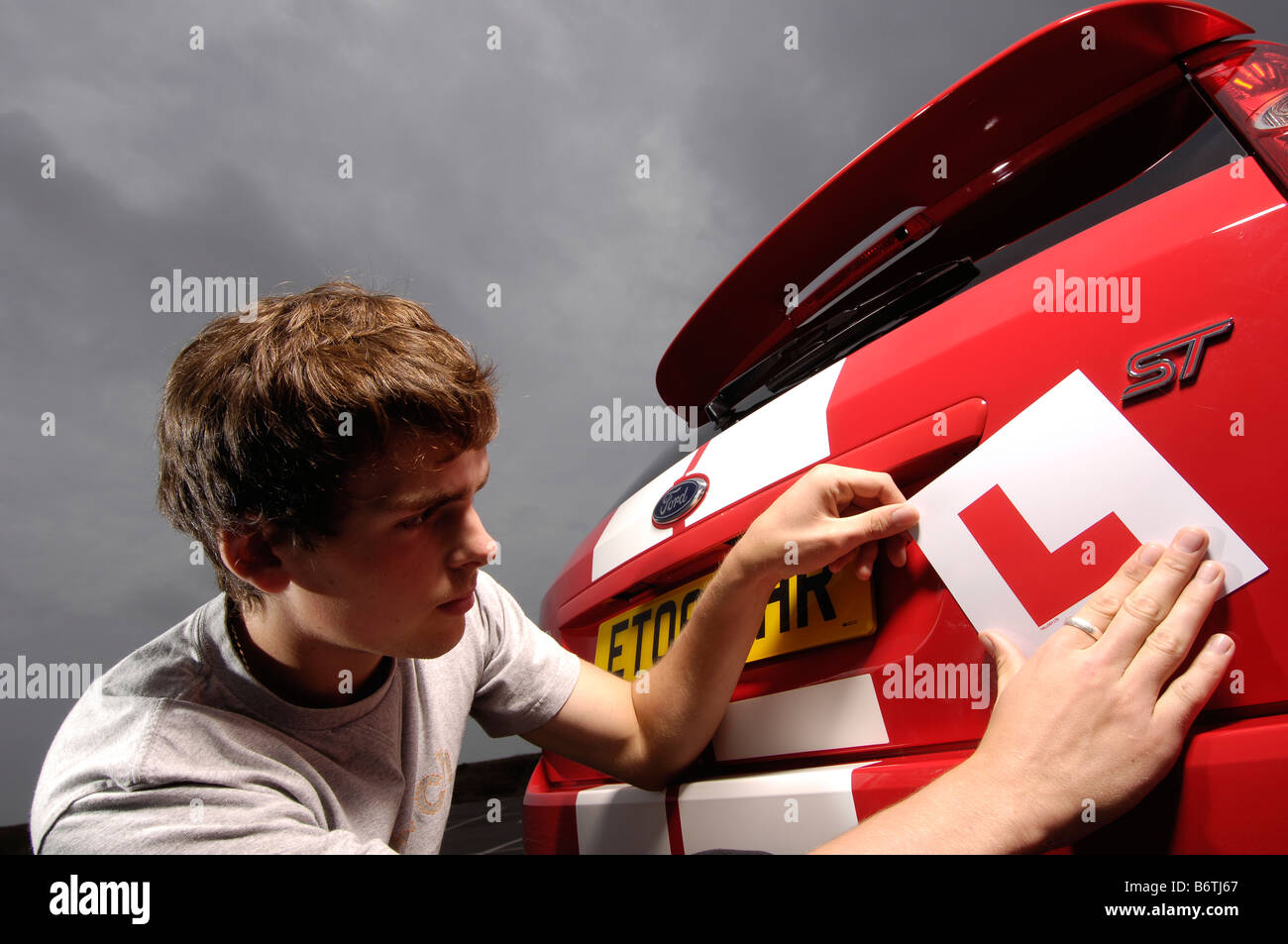 Learner driver, puts l  plates on  red car Stock Photo
