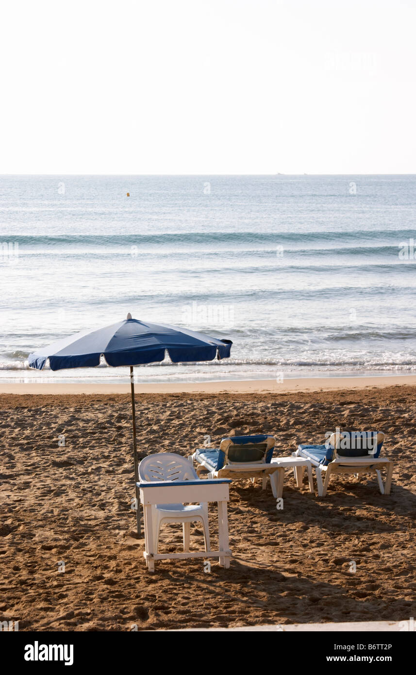 The beach. Two empty deck chairs and a parasol. A plastic chair and