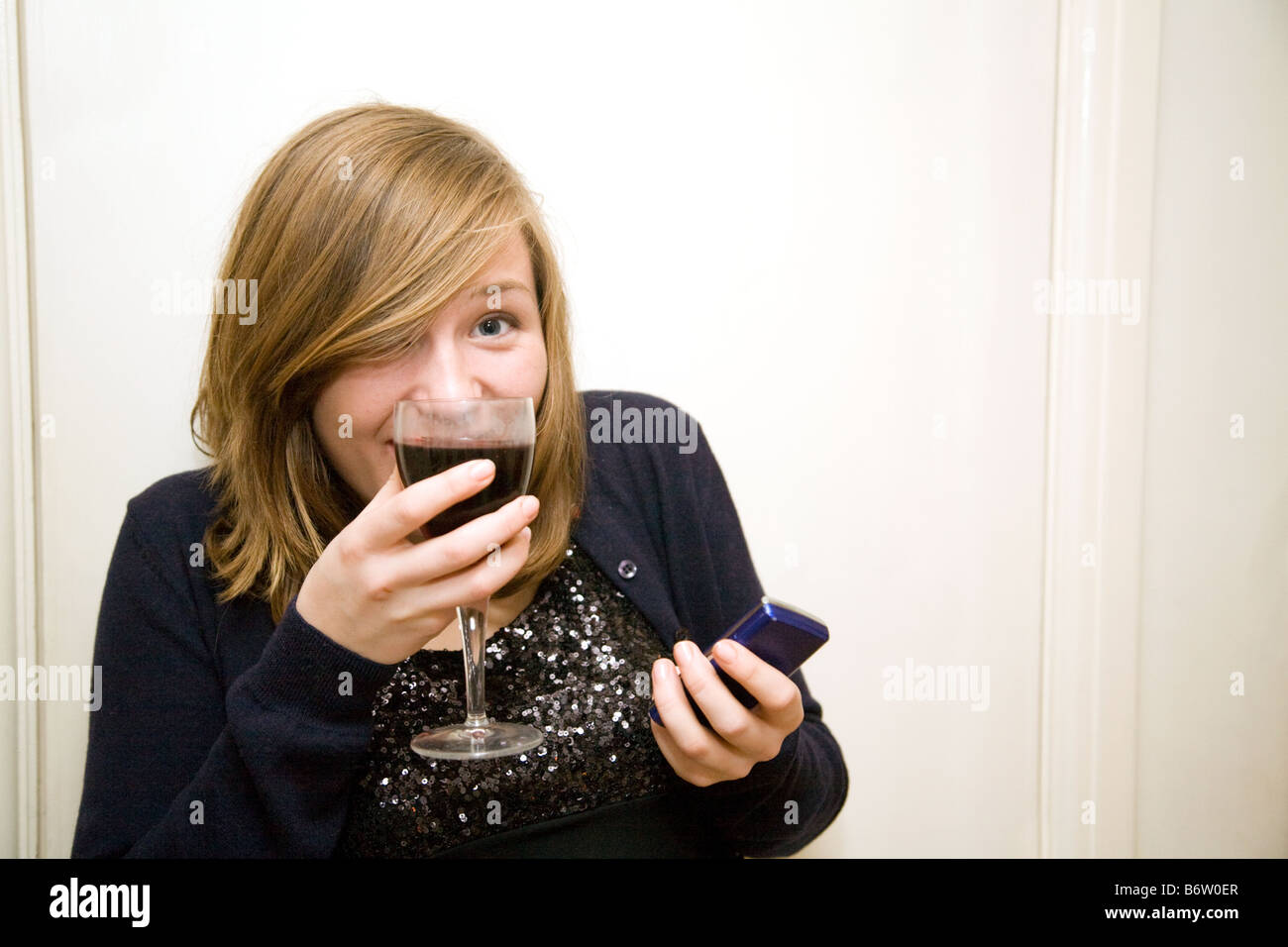 Blonde teenage girl age aged 14-15 years old drinking wine and texting with her mobile phone, UK Stock Photo