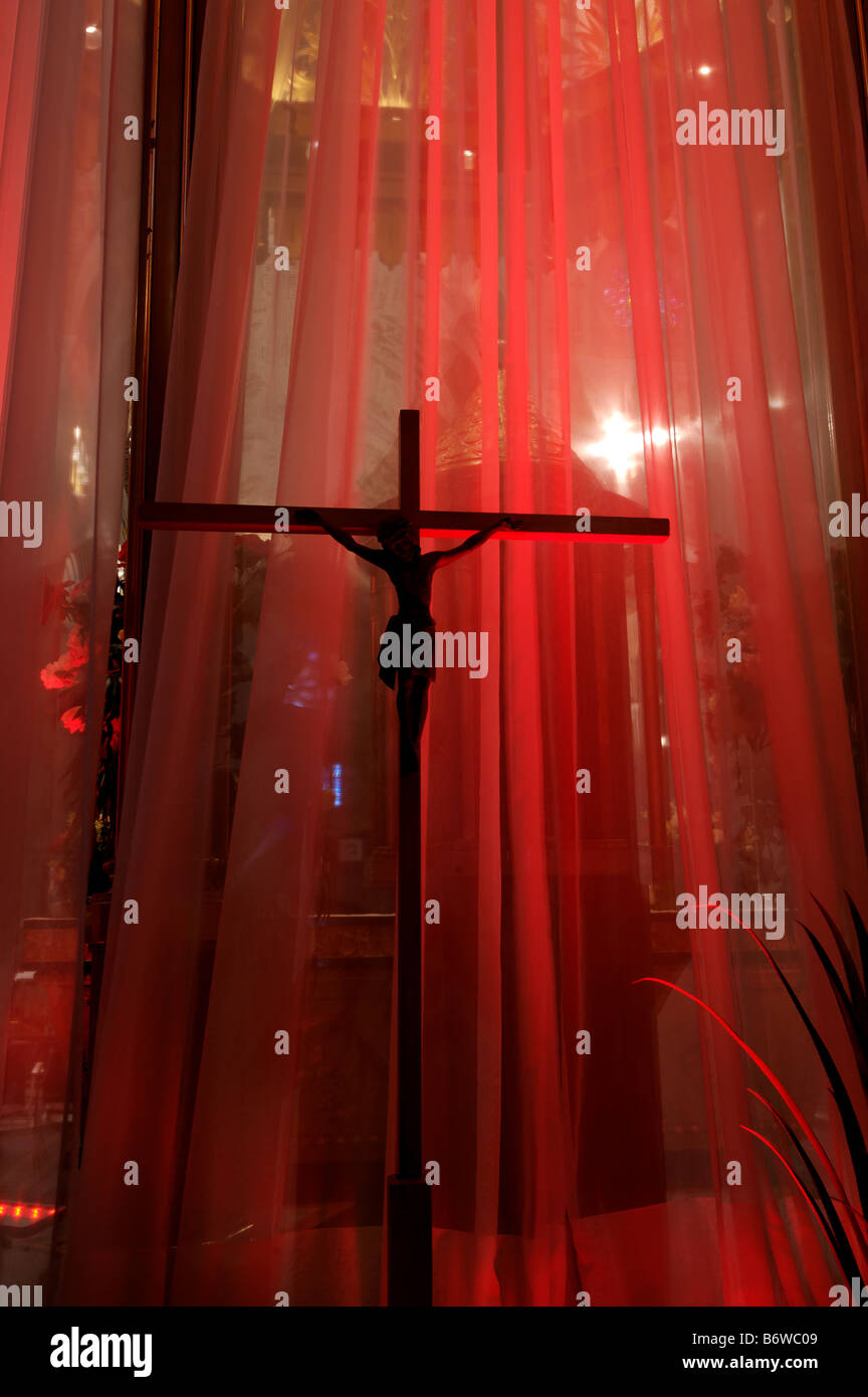 A statue of jesus on the cross silhouetted against a red curtain in a church Stock Photo