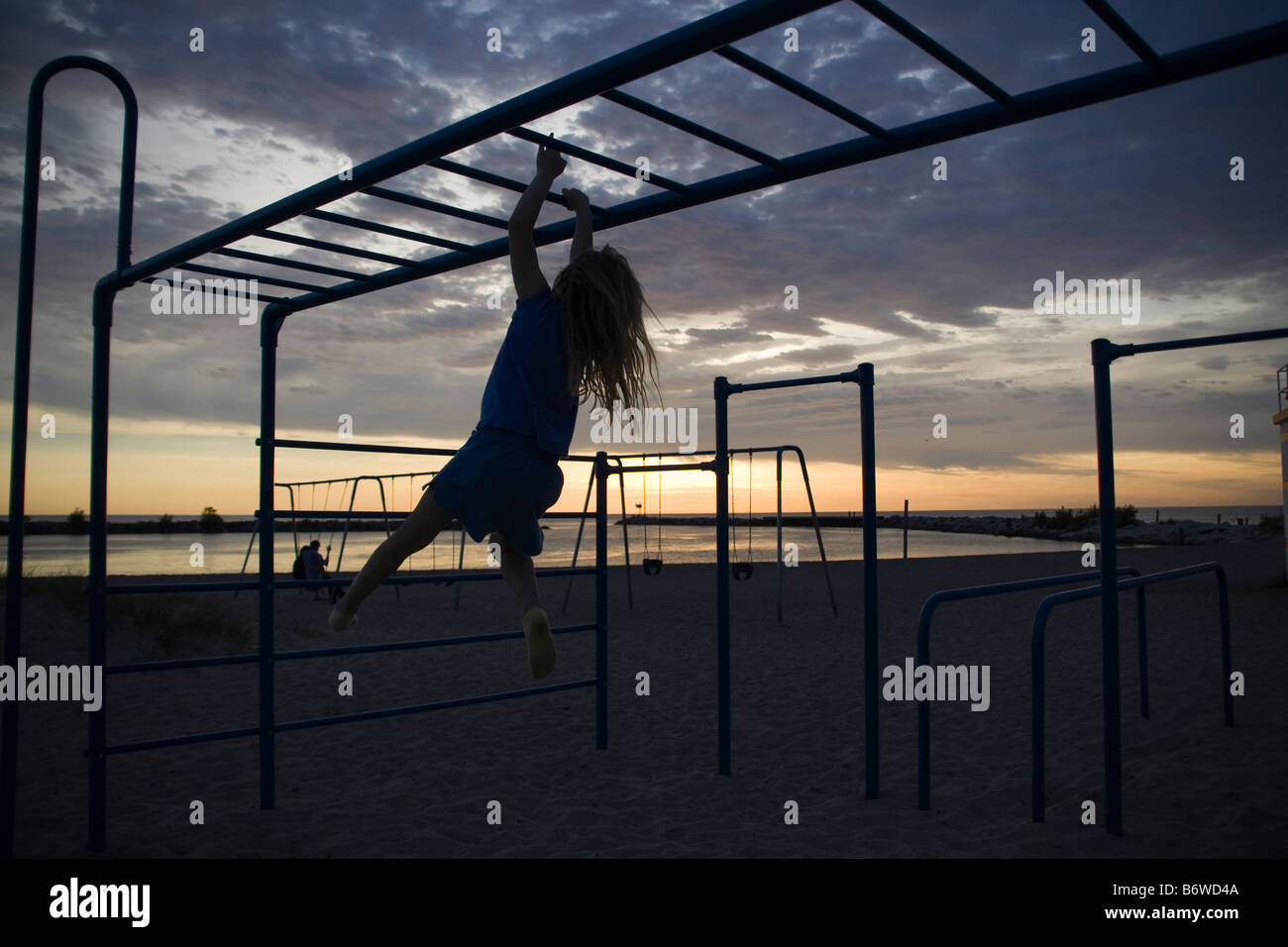 Girl swinging on monkey bars at park on beach at dusk Stock Photo