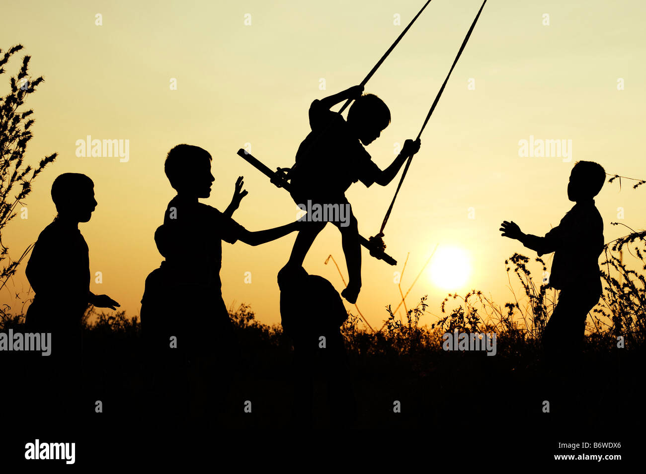 Silhouette of Indian children playing on a home made swing in the countryside at sunset. Andhra Pradesh, India Stock Photo