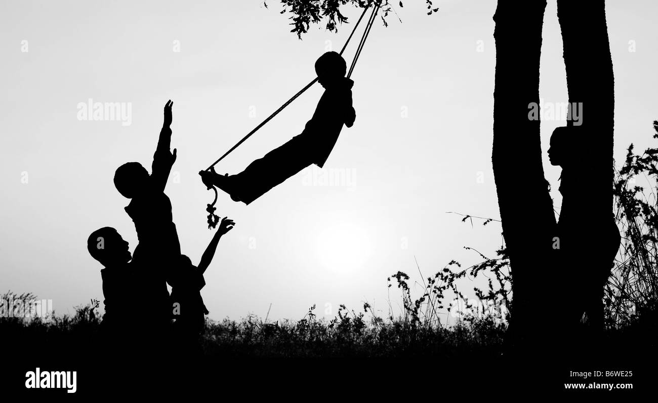 Silhouette of Indian children playing on a home made swing in the countryside at sunset. Andhra Pradesh, India Stock Photo