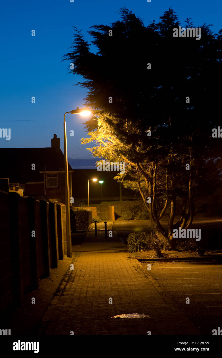 deserted empty footpath in a town at night illuminated by lights from lamppost UK - nobody no people Stock Photo