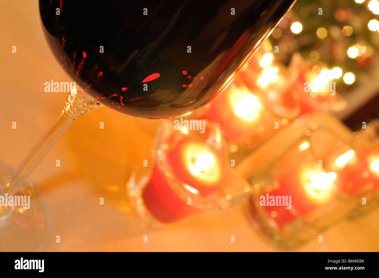 Abstract concept with glass filled with red wine and red votive candles lit on table in front of Christmas lights and tree. Stock Photo