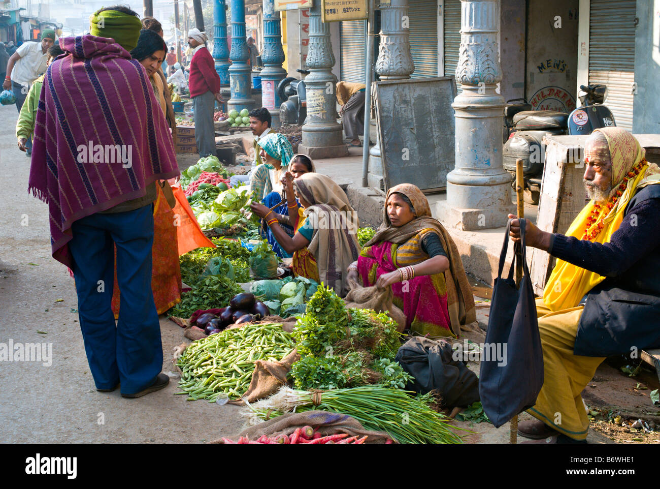 INDIA VARANASI Indian women in colorful saris selling beautiful vegetables on the street in Varanasi as an elderly Sadu waits Stock Photo