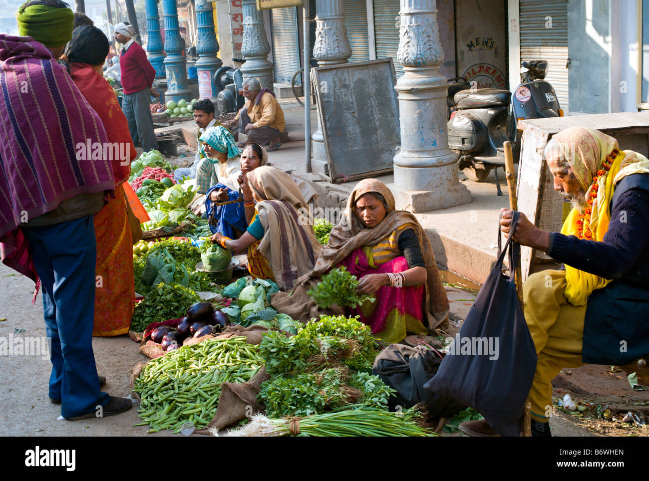 INDIA VARANASI Indian women in colorful saris selling beautiful vegetables on the street in Varanasi as an elderly Sadu waits Stock Photo