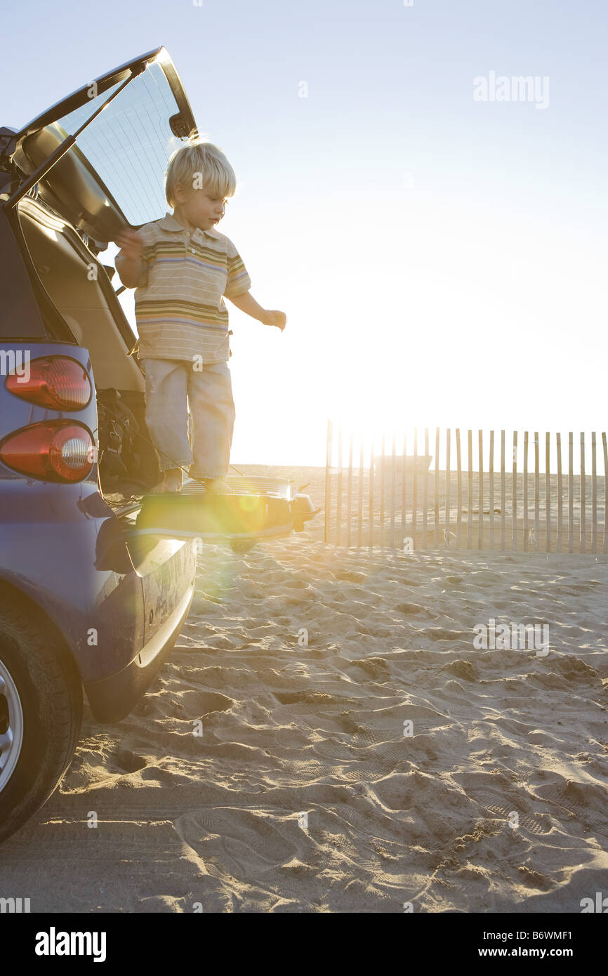 Young boy standing on rear of Smartcar at beach Stock Photo