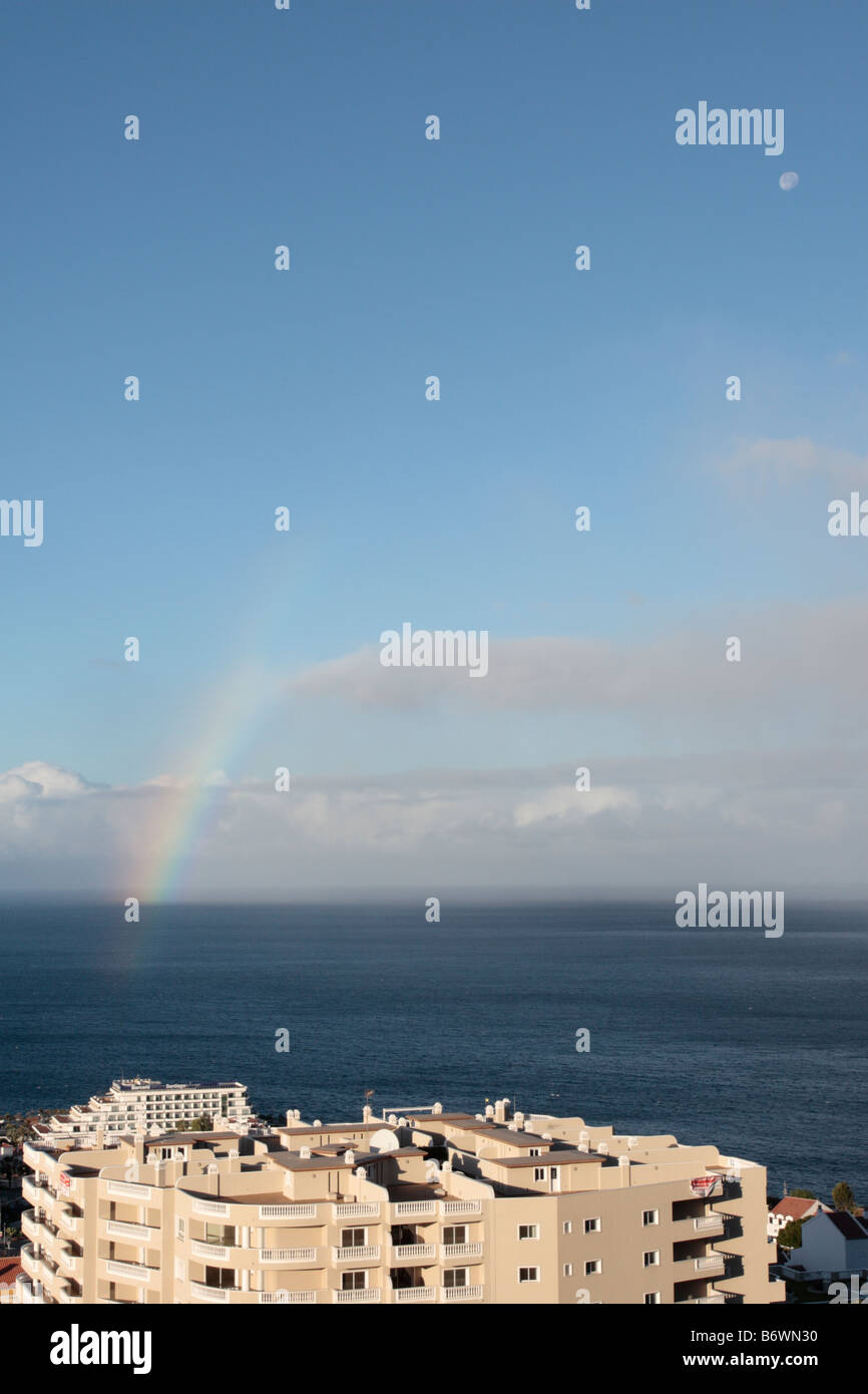 A rainbow at sea off the coast of Tenerife with the hotel Barcelo Santiago and a large apartment block in the foreground Stock Photo