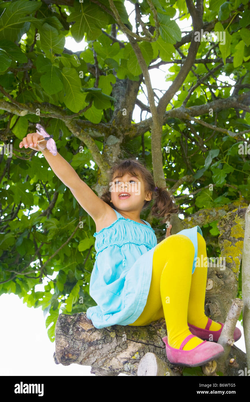 Маленькая девочка в юбке лазает на дереве. Девочка пробралась. Девочка не может залезть на горку. Дерево для детей. Девочка карабкается на дерево.