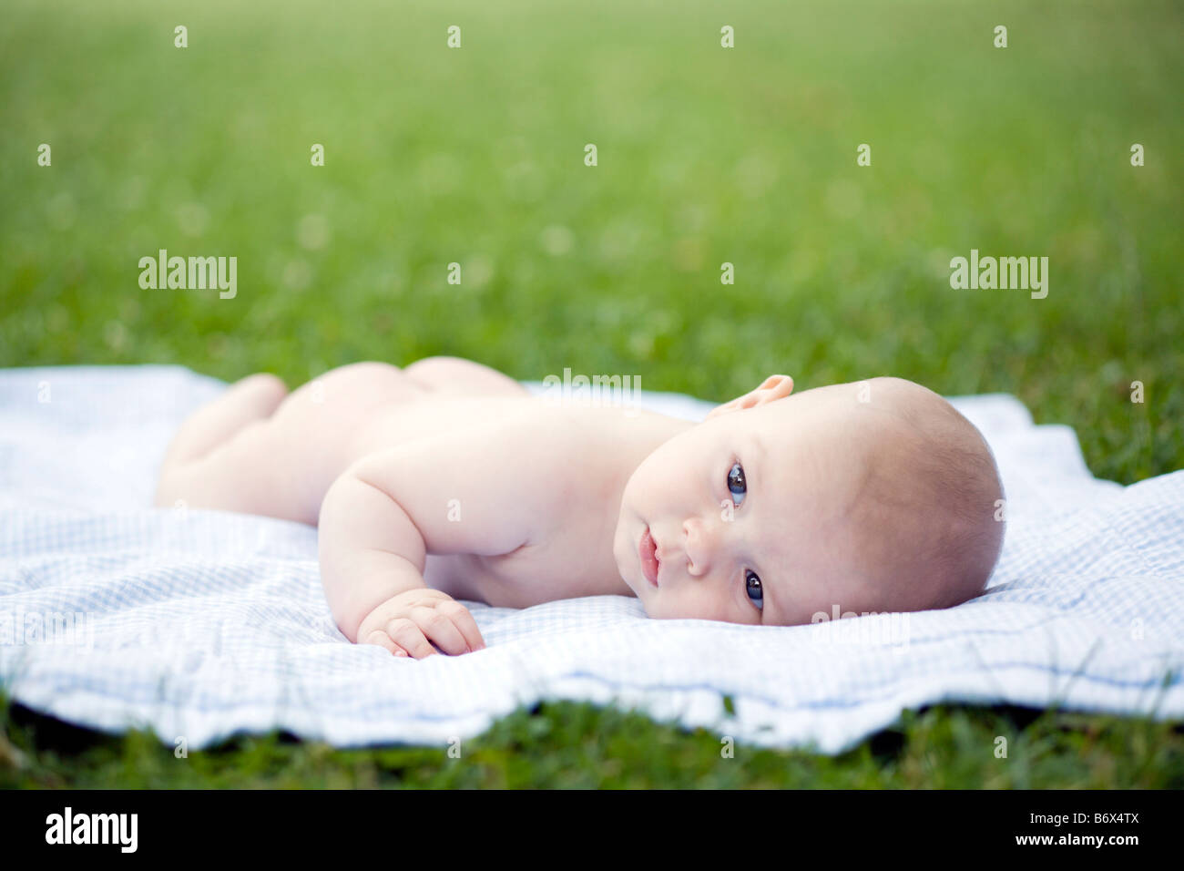 a baby laying alone on a blanket in a park Stock Photo