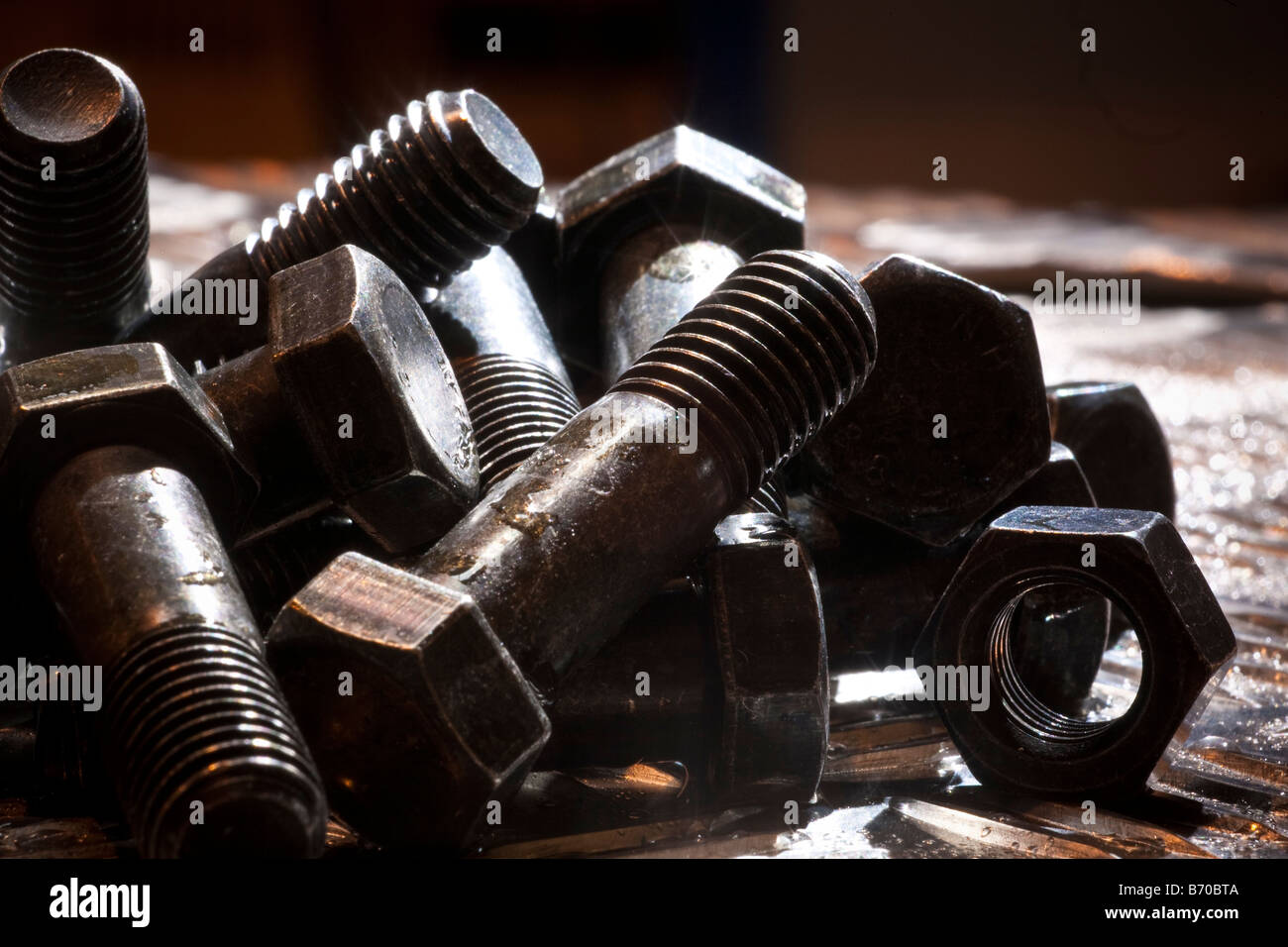 Random  artistic pile of threaded bolts and a  hexagonal nut on a sheet steel, backlit. Stock Photo