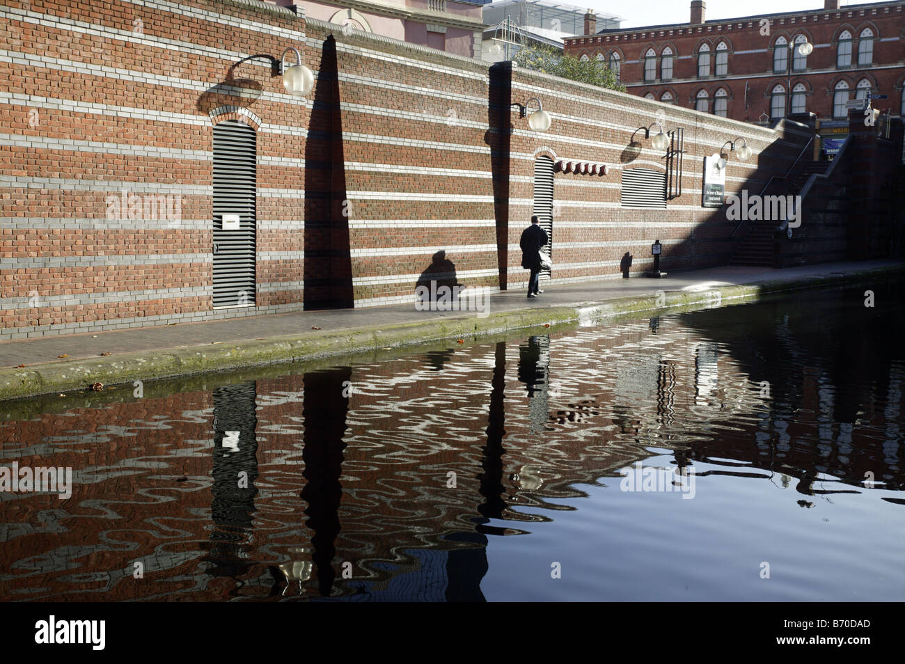 A pedestrian walks along a towpath leading under Broad Street towards Gas Street canal basin in Birmingham UK Stock Photo