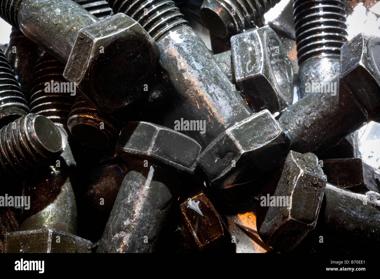 Random  artistic pile of threaded bolts on a sheet steel, backlit. Stock Photo