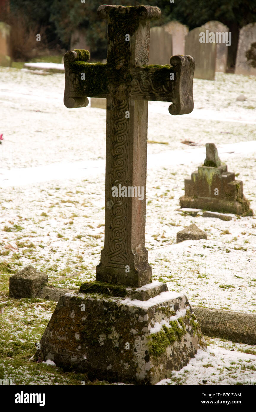 A stone cross covered in Celtic knot carving in a snowy graveyard Stock Photo