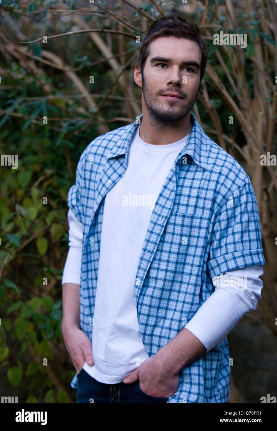 man attractive in green garden wearing white t-shirt and blue checked shirt Stock Photo