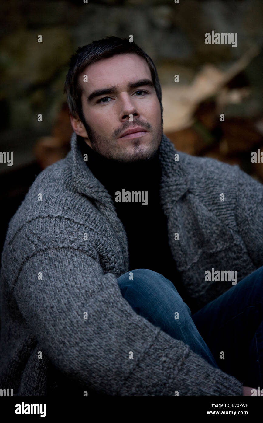 man outside wearing wooly cardigan log pile in background Stock Photo