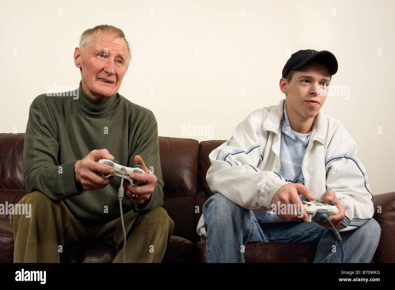 A teenager playing on a games console (xbox 360) with a elder man Stock Photo